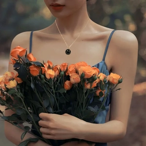 Detail of a gold necklace with a black smiley face charm worn by a model with roses