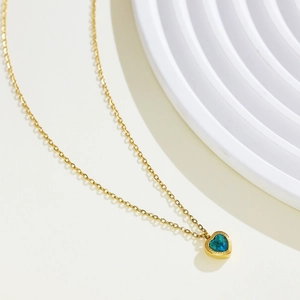 Close-up of a 18k gold heart pendant with a sparkling blue zircon on a white background
