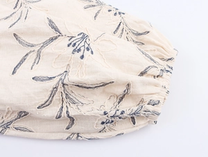 Detailed close-up of blue floral embroidery on creamy white cotton-linen fabric sleeve