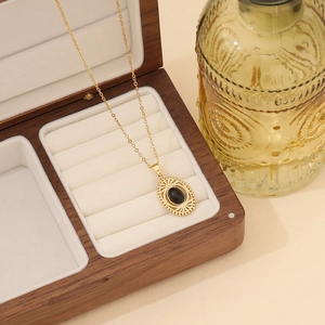 Golden necklace with black stone oval pendant in a wooden jewelry box on white velvet