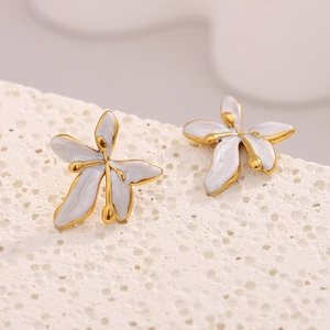 Macro shot of white enamel flower stud earring with gold edges on stone background