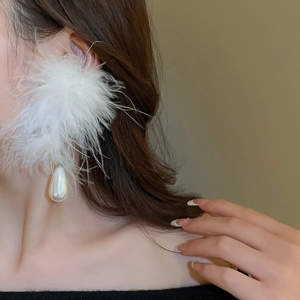 Detailed close-up of white feather earrings with elegant teardrop pearl pendant on model