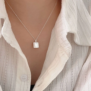 Macro detail of minimalist silver square pendant necklace worn on a textured shirt