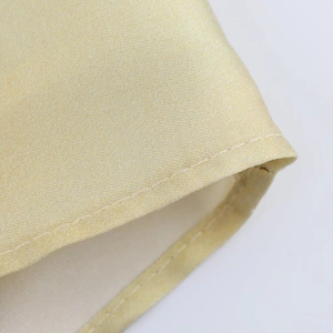 Vue macro du tissu satiné doré champagne avec couture détaillée sur l'ourlet du vêtement