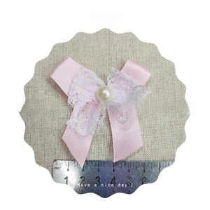 Pink ribbon bow with white lace and center pearl detail shown with scale reference