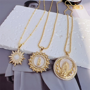 Detail of 18k gold religious pendants with pearls and zircons on a white stone base