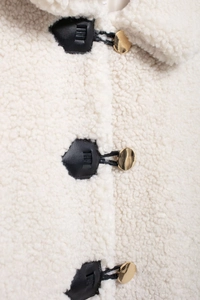Dettaglio giacca in pile bianco con inserti in pelle nera e bottoni dorati