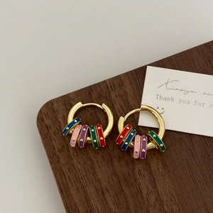 Detail of gold hoop earrings with colorful dotted charms on a vintage wood surface
