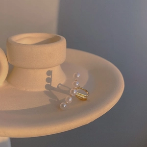 Detail of minimalist gold ear cuff featuring five linear pearls on a ceramic tray