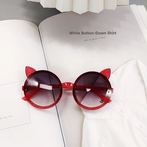 Detail of red glitter cat-ear sunglasses with purple gradient lenses on a magazine