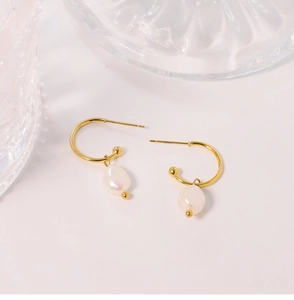 Macro detail of C-shaped gold hoop earrings with white baroque pearl pendants