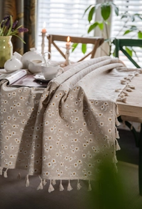 Detail of floral linen tablecloth with beige tassels and daisy prints on a wooden table