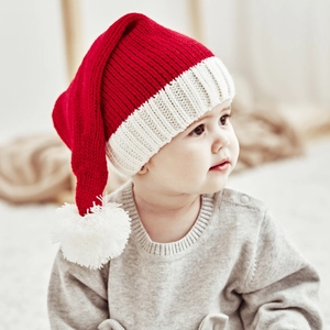 Close-up of a baby wearing a red Christmas knit hat with a white pompom and soft trim