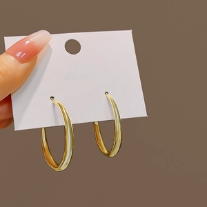 Close-up of a large smooth golden hoop earring held against a clean brown background