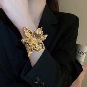 Detail of a large gold sculptural flower cuff bracelet on a black blazer sleeve