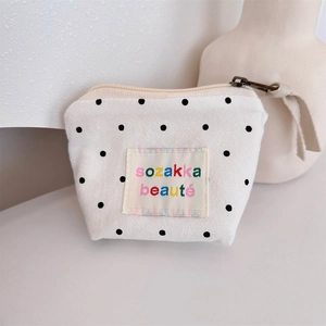 Detailed close-up of a cream canvas pouch with black polka dots and vintage bronze zipper
