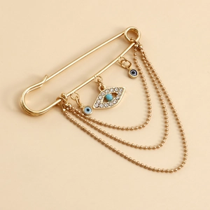 Detailed view of a gold safety pin brooch with sparkling evil eye charms and tassels