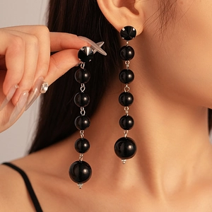 Close-up of black beaded drop earrings with geometric studs and layered spheres