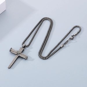 Détail d'un pendentif croix en acier titane avec trois clous, nœud torsadé et chaîne box
