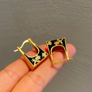 Vintage U-shaped gold earrings with black enamel and floral pattern held by fingers