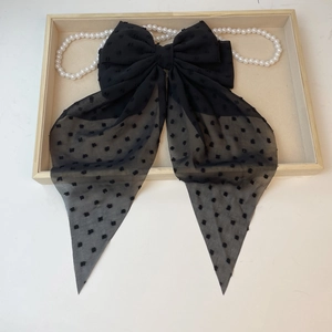 Detail of a large black chiffon bow hair clip with velvet polka dots and long ribbons