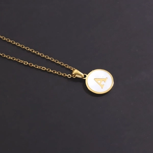 Macro detail of 18k gold plated round shell pendant featuring the engraved letter A