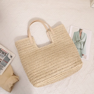 Large beige woven straw tote bag with brown handles on a textured background for beach vacation
