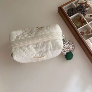 Close-up of quilted cream pouch with floral embroidery and a cute mushroom zipper pull