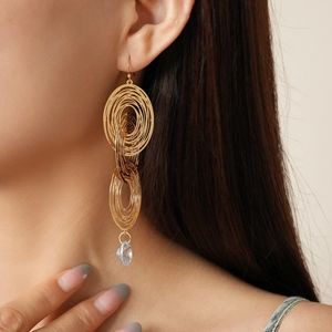Macro side view of golden multilayer oval hoop earrings with a clear teardrop crystal