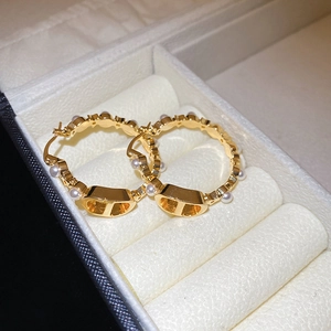 Macro detail of gold plated hoop earrings with pearls and designer letter charm