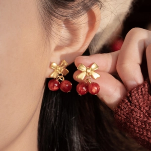 Elegant red cherry stud earrings with golden bow detail on model for fashion look