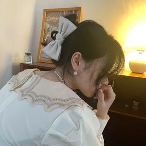 Detail of cream silk bow hair claw clip worn by a model in warm home lighting