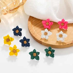 Colorful matte floral earrings in pink, white, and yellow on a rustic wooden tray
