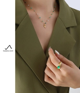 Detail of tulip pendant necklace and green gemstone ring on olive green suit