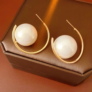 Close-up of vintage C-shaped gold hoop earrings with large white pearls on a jewelry box