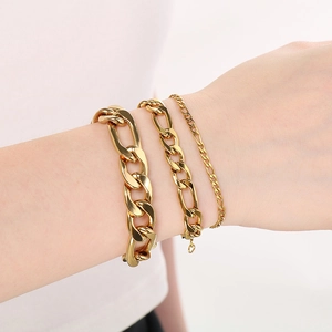 Detailed view of layered gold stainless steel Figaro and curb link bracelets on a wrist