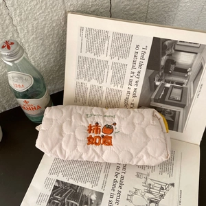 Quilted floral pencil case with persimmon embroidery and yellow zipper on a magazine