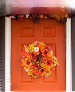 Detail of harvest wreath with maple leaves, sunflowers and pumpkins on orange door