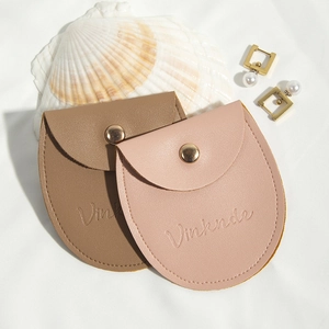 Brown and pink PU leather jewelry pouches with snap buttons on elegant white fabric background