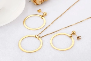 Detailed close-up of golden hollow geometric necklace and earring set on white fabric