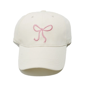 Close-up of a cream baseball cap featuring detailed pink bow embroidery and cotton texture