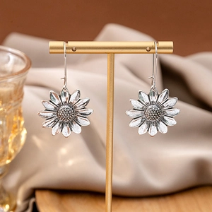 Detailed view of antique silver sunflower drop earrings on a golden display stand