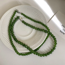 Detailed view of a dark green beaded necklace with silver clasp on white ceramic tray
