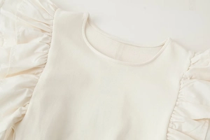 Detailed view of the ruffle trim and rib-knit texture on a cream white round-neck top