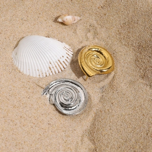 Dettaglio di orecchini a spirale oro e argento sulla sabbia con conchiglie