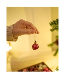 Close-up of small glossy red Christmas ball ornament with gold cap and string on tree
