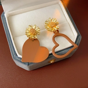 Detailed close-up of daisy studs and asymmetric heart charms in a blue jewelry box