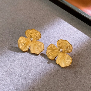 Macro shot of gold clover earrings with fine texture and center crystals on gray stone