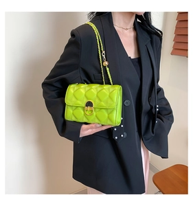 Detail of neon green quilted crossbody bag with gold chain strap worn on black blazer
