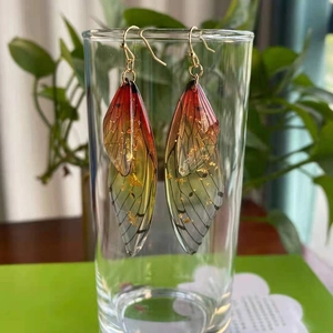 Macro detail of red and yellow gradient cicada wing earrings with gold foil accents